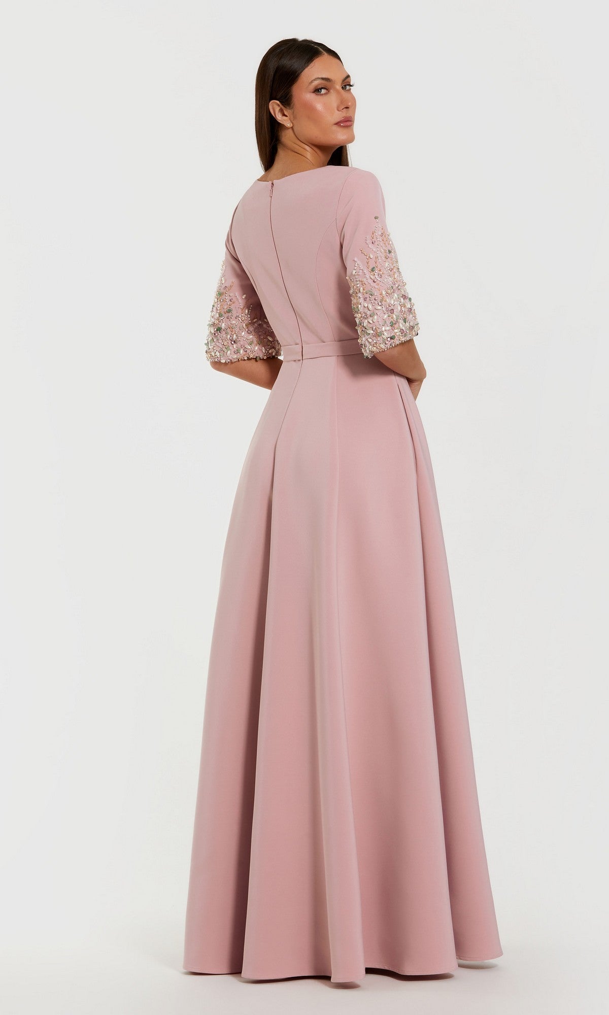 A woman stands facing away, wearing the Mac Duggal 2322 Long Formal Dress in light pink crepe, with three-quarter embellished sleeves and an elegant A-line skirt.